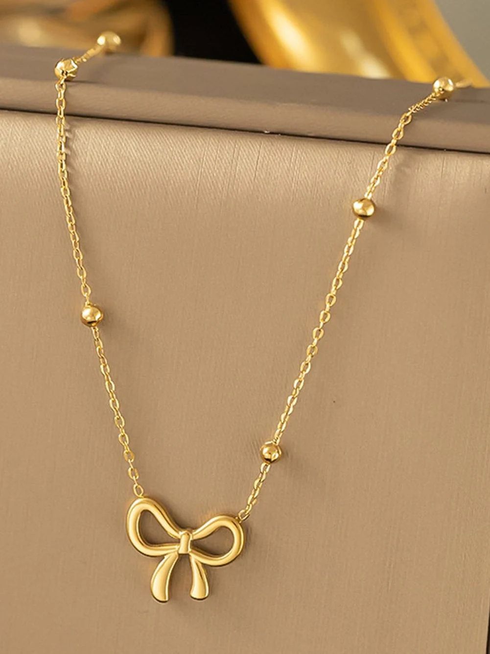 Gold bow-shaped necklace on a beige surface