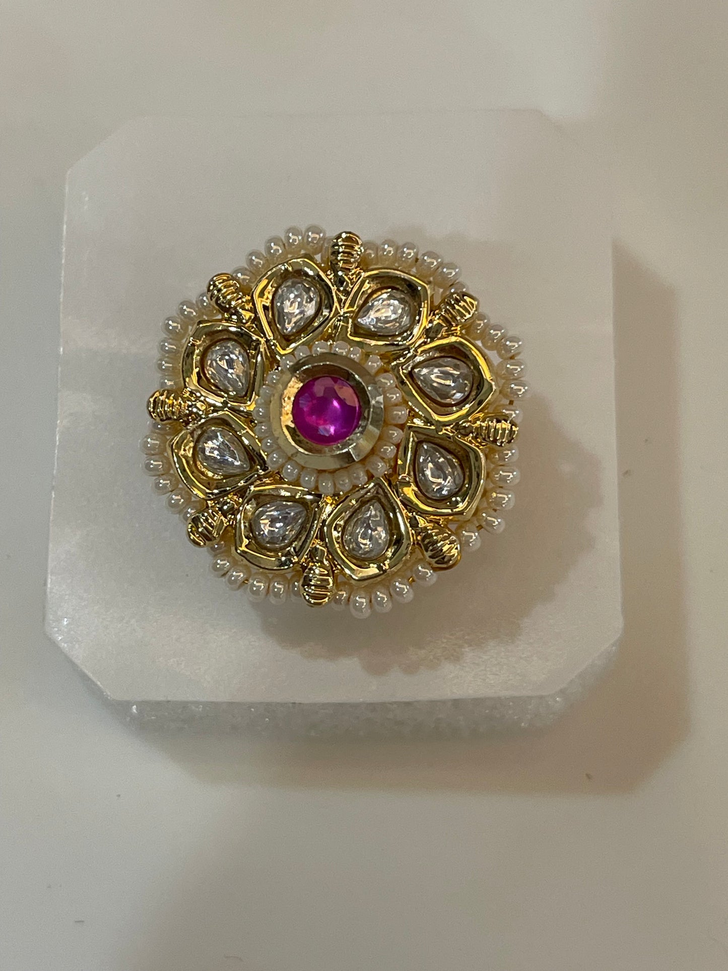 Golden Kundan ring with a central ruby stone surrounded by petal shaped gemstones and white beads.